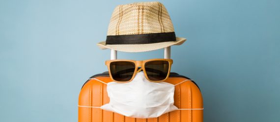 Suitcase with hat, sunglasses and protective medical mask on pastel blue background minimal creative coronavirus covid-19 travel concept.
