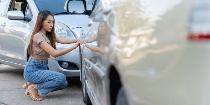 Asian woman inspecting the damage after a car accident