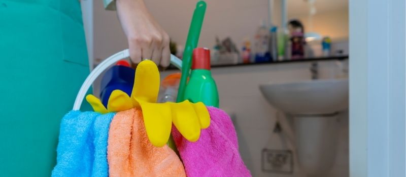Domestic helper holding a bucket of cleaning tools and liquids