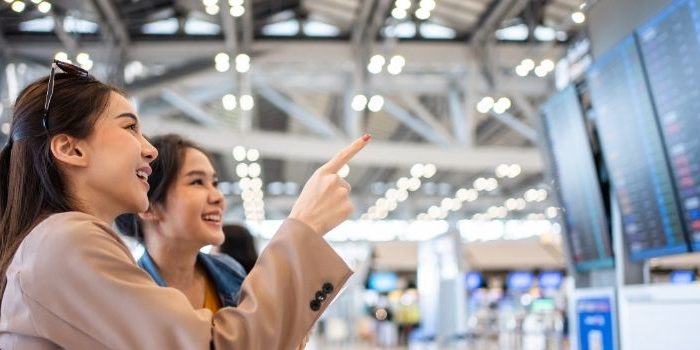 Two smiling ladies looking at flight timings at the airport