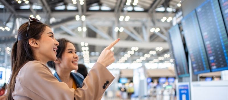 Two smiling ladies looking at flight timings at the airport