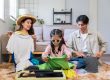 A girl packing her own clothes with her parents at the back, as part of their travel essentials list