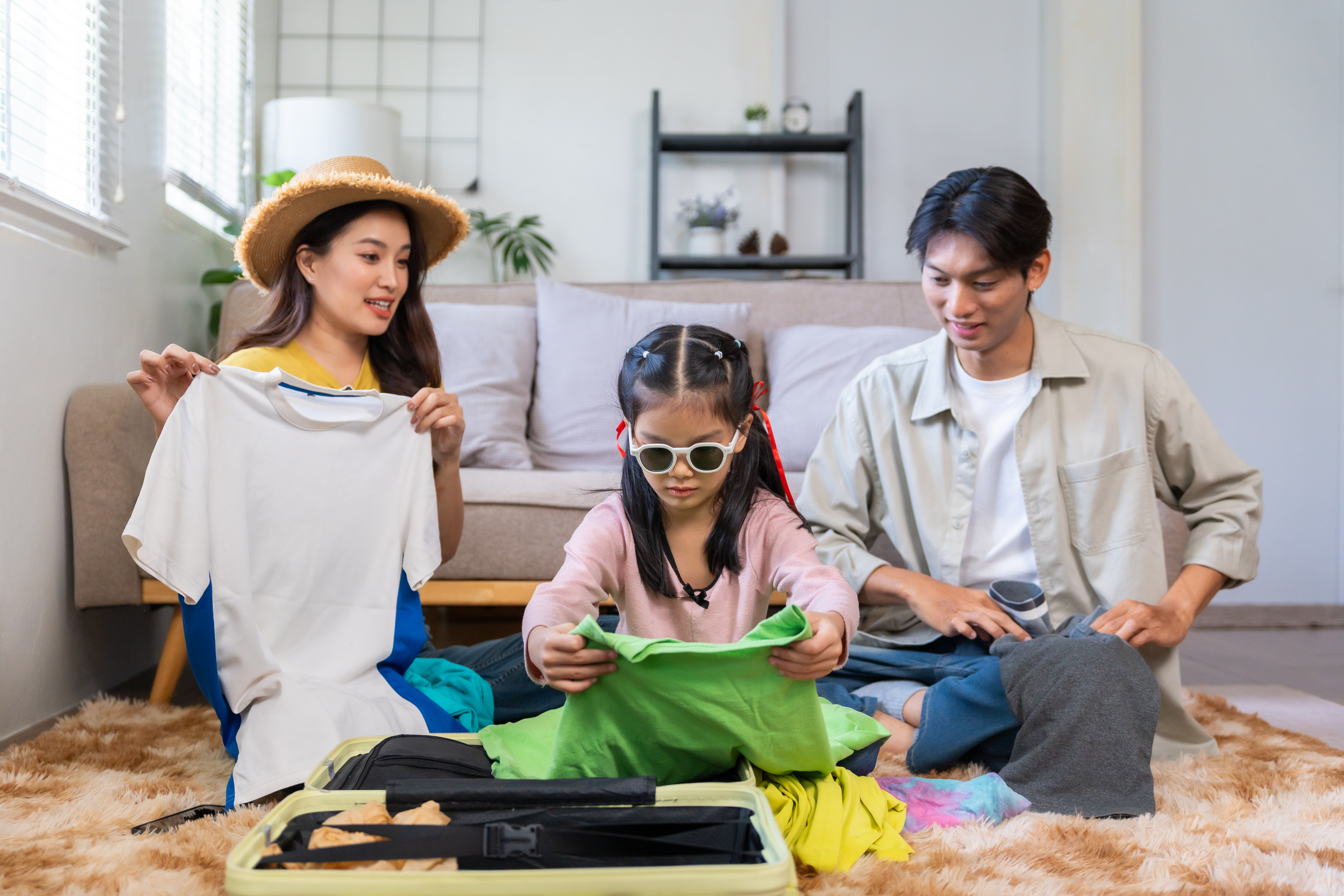 Asian family packing suitcase for summer travel vacation A girl packing her own clothes with her parents at the back, as part of their travel essentials list