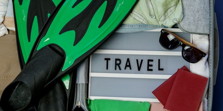 an open suitcase with water sports equipment, beach clothes, sunglasses, and a board that says TRAVEL